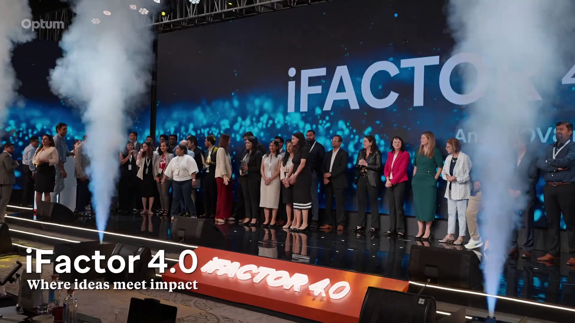 Full group photograph on stage with CO2 jets under the iFactor 4.0 “Where ideas meet impact” backdrop